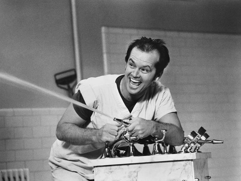 Schwarz-Weißaufnahme von Jack Nicholson, wie er mit einem Wasserschlauch spritzt und sich dabei amüsiert.
