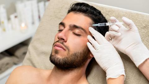 Ein junger Mann liegt auf einer Liege und lässt sich Botox in die Stirn spritzen