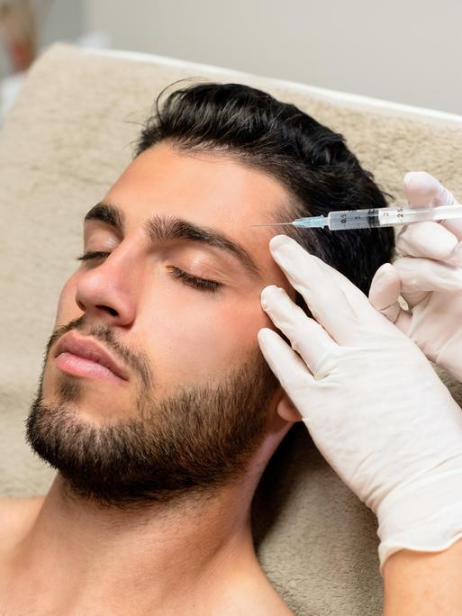 Ein junger Mann liegt auf einer Liege und lässt sich Botox in die Stirn spritzen