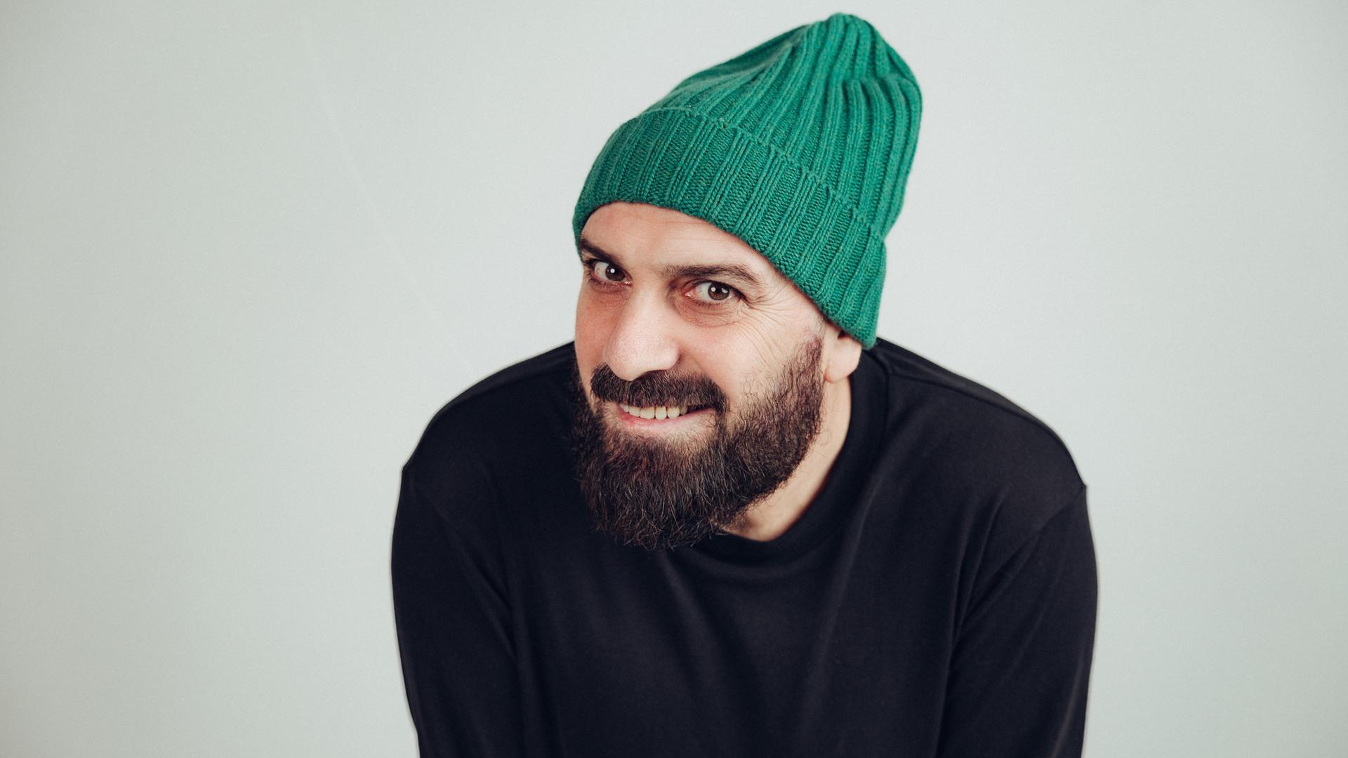 Delschad Numan Khorschid lächelt in die Kamera. Er trägt einen akkurat gestutzten Vollbart und eine knallgrüne Strickmütze. Delschad Numan Khorschid lächelt in die Kamera. Er trägt einen akkurat gestutzten Vollbart und eine knallgrüne Strickmütze.