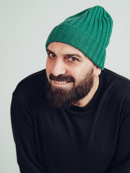Delschad Numan Khorschid lächelt in die Kamera. Er trägt einen akkurat gestutzten Vollbart und eine knallgrüne Strickmütze.