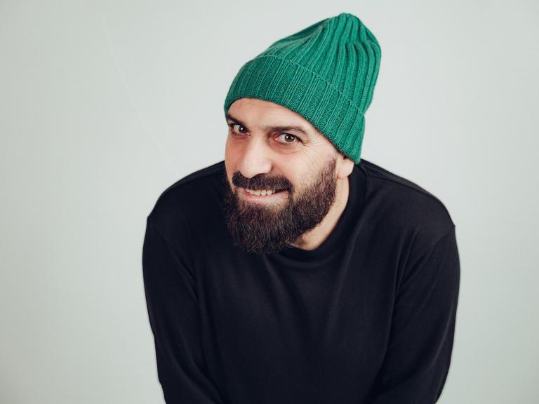Delschad Numan Khorschid lächelt in die Kamera. Er trägt einen akkurat gestutzten Vollbart und eine knallgrüne Strickmütze.