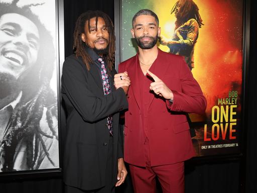 Sheldon Shepherd (links) und Hauptdarsteller Kingsley Ben-Adir stehen vor zwei Plakaten: Das linke zeigt Bob Marley lachend, das rechte ist ein Filmplaket für den Film "Bob Marley - One Love" von Reinaldo Marcus Green. Ben-Adir trägt seine Haare kurz, er hat einen roten Anzug an. Shepherd hat lange Dreadlocks und trägt einen schwarzen Mantel, schwarzes Hemd und bunte Krawatte.