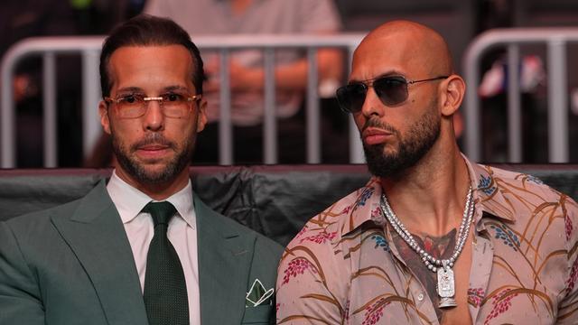 Andrew Tate (rechts) sitzt mit Sonnenbrille bei einer Veranstaltung in Miami neben seinem Bruder Tristan, der eine klare Brille trägt.