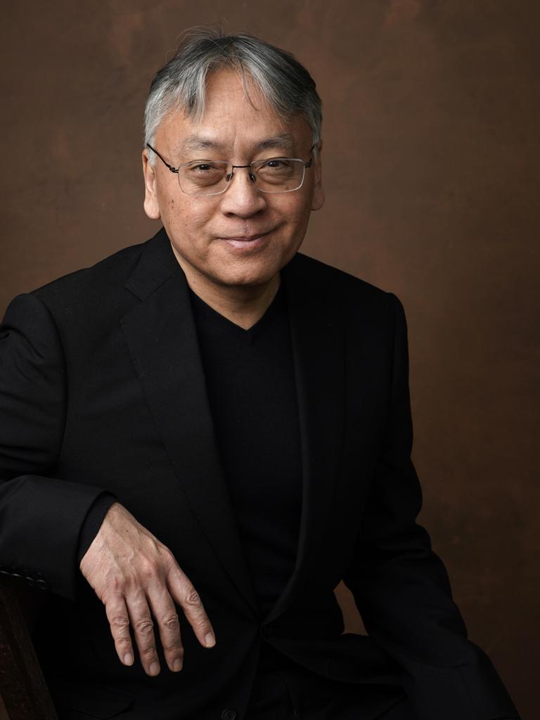 Kazuo Ishiguro sitzt vor neutralem Hintergrund und lächelt in die Kamera.