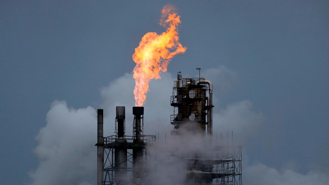 Aus den von Dampf umgebenen Aufbauten einer Industrieanlage steigt eine offene Flamme auf.