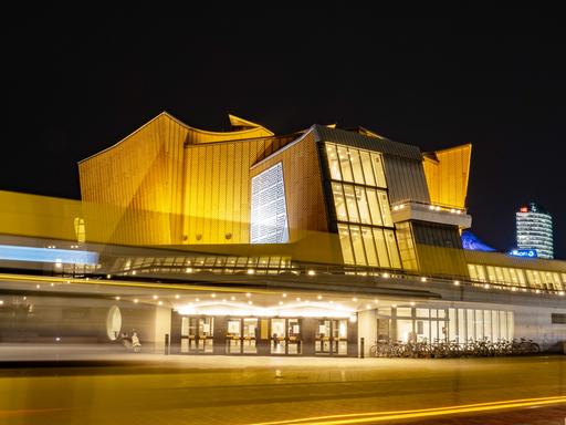 Die Berliner Philharmonie bei Nacht: Nur als Lichtstreifen zu erkennen ist, bei einer Langzeitbelichtung, ein Linienbus, der am späten Abend an der Philharmonie vorbeifährt. Sie zählt zu den wichtigsten Konzertsälen Berlins.