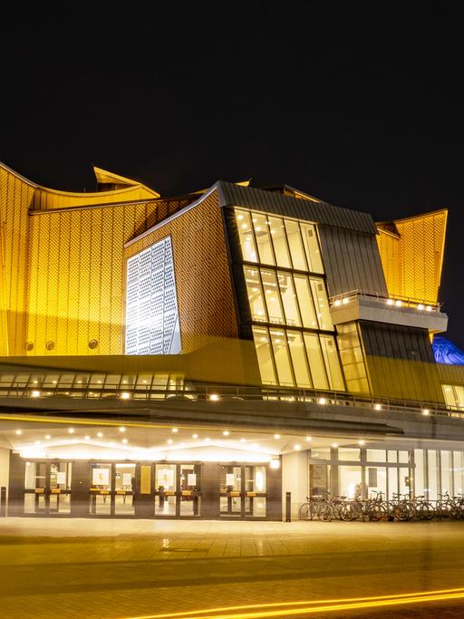 Die Berliner Philharmonie bei Nacht: Nur als Lichtstreifen zu erkennen ist, bei einer Langzeitbelichtung, ein Linienbus, der am späten Abend an der Philharmonie vorbeifährt. Sie zählt zu den wichtigsten Konzertsälen Berlins.