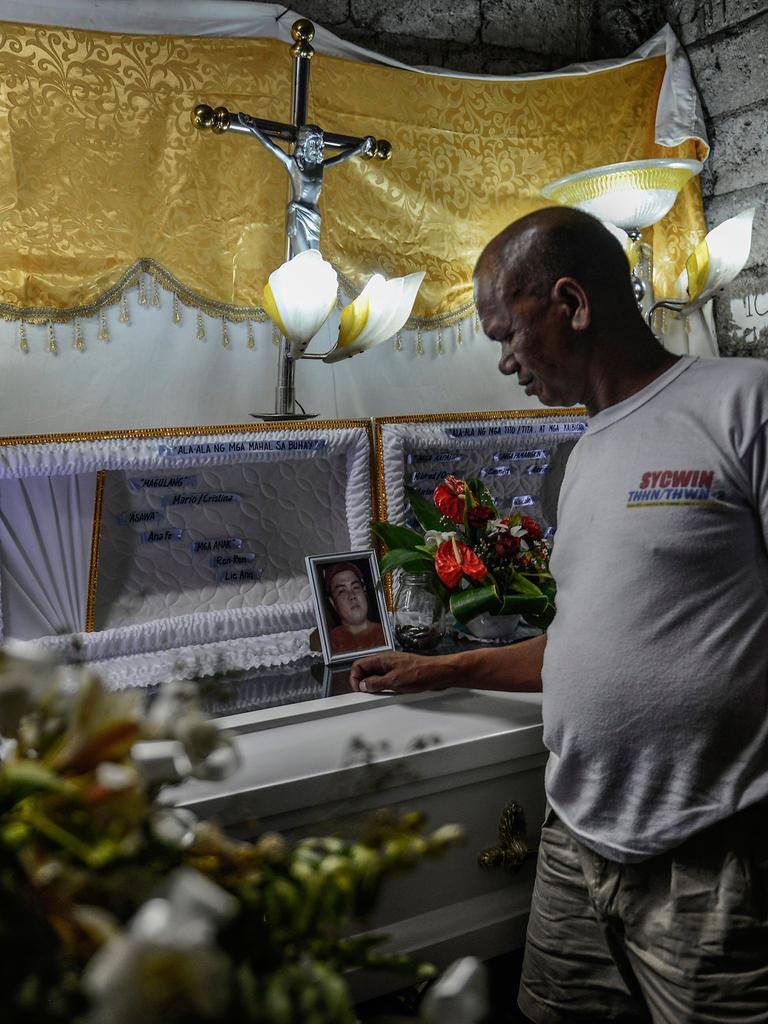 Ein Mann steht an einem Sarg, auf dem das Porträt eines jungen Mannes zu sehen ist.