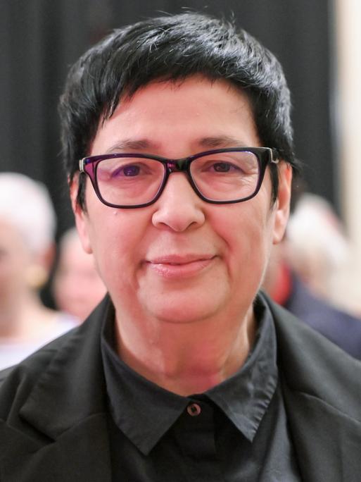 Seyran Ateş blickt lächelnd und geradeaus in die Kamera. Sie trägt eine schwarze Brille und ein schwarzes Hemd.