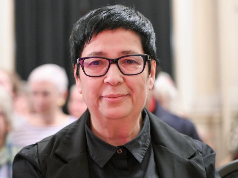 Seyran Ateş blickt lächelnd und geradeaus in die Kamera. Sie trägt eine schwarze Brille und ein schwarzes Hemd.