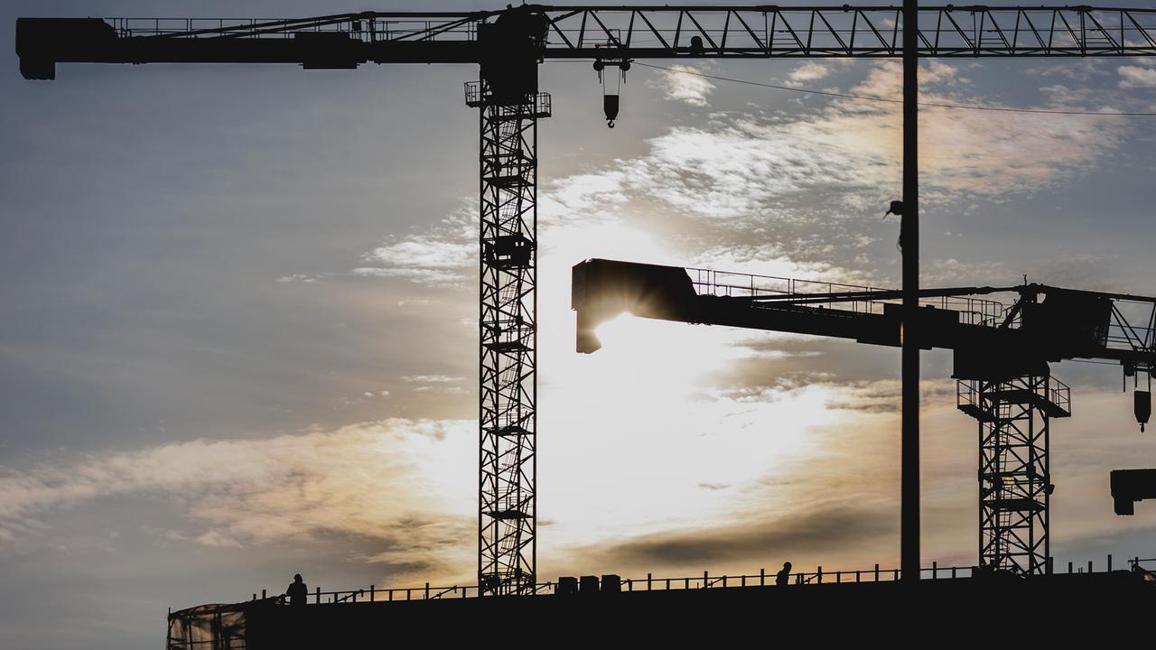 Zwei Bauarbeiter zeichnen sich ab als Silhouette an einem Baugerüst vor der untergehenden Sonne.