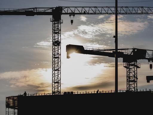 Zwei Bauarbeiter zeichnen sich ab als Silhouette an einem Baugerüst vor der untergehenden Sonne.