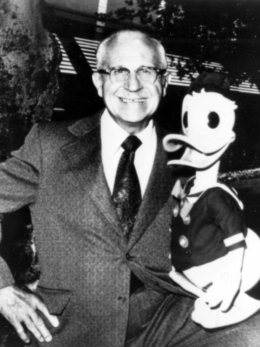 Schwarz-weiß-Aufnahme von Clarence Nash, der die Figur Donald Duck im Arm hält und lächelt 