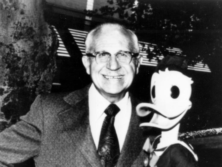Schwarz-weiß-Aufnahme von Clarence Nash, der die Figur Donald Duck im Arm hält und lächelt 