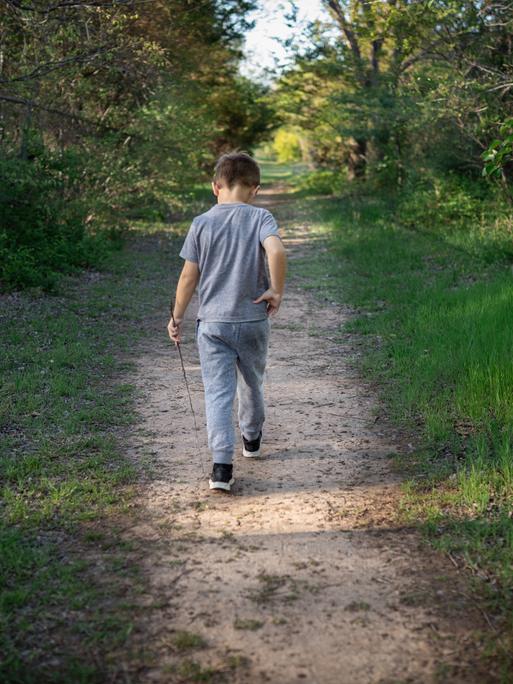 Ein etwa zehnjähriger Junge wandert alleine durch den Wald. Es ist nur sein Rücken zu sehen.