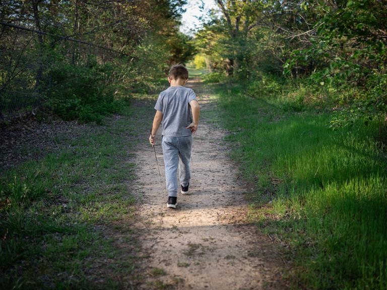 Ein etwa zehnjähriger Junge wandert alleine durch den Wald. Es ist nur sein Rücken zu sehen.