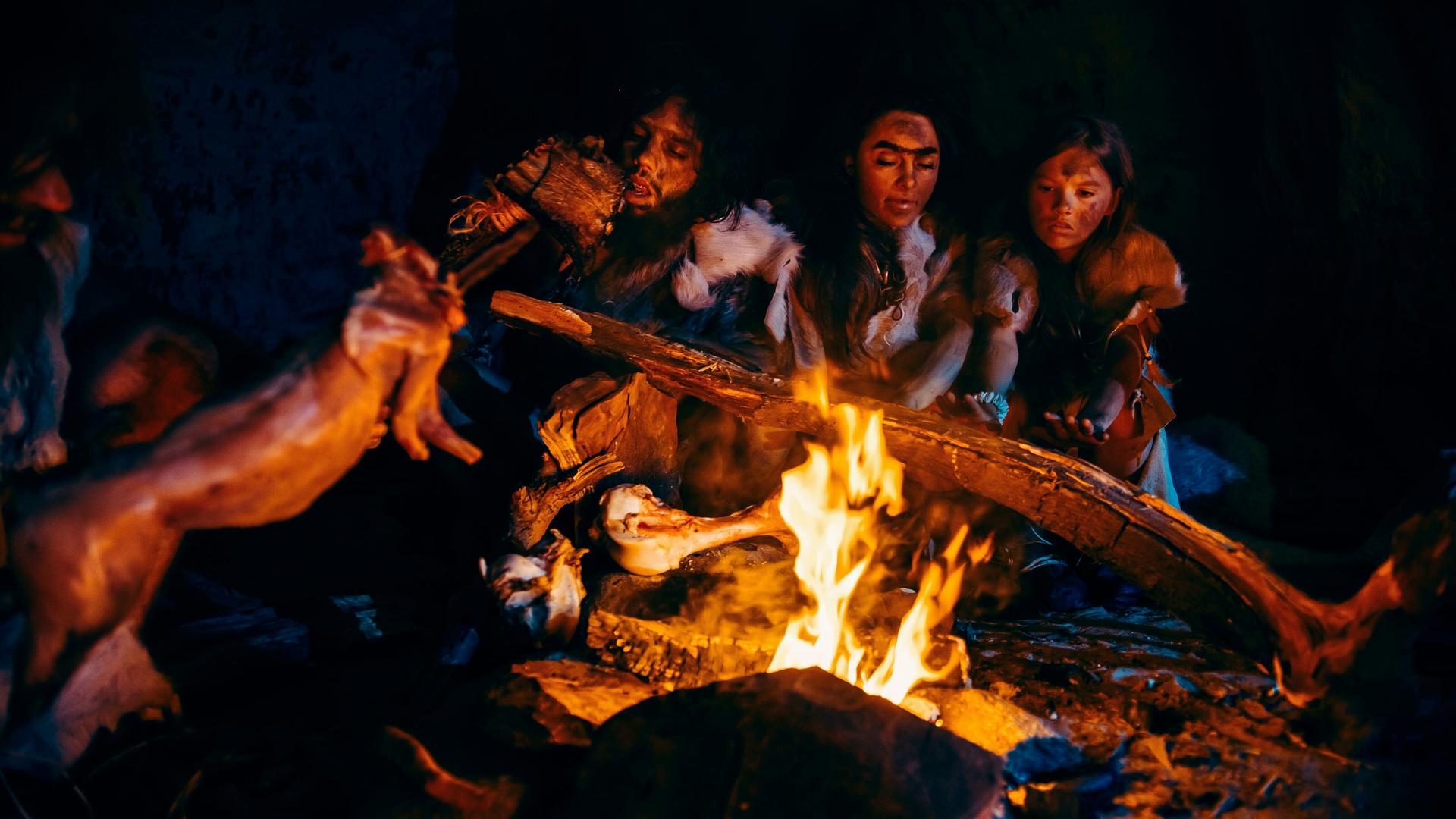 Neandertaler braten über einem offenen Feuer Fleisch in einer Höhle. Neandertaler braten über einem offenen Feuer Fleisch in einer Höhle.