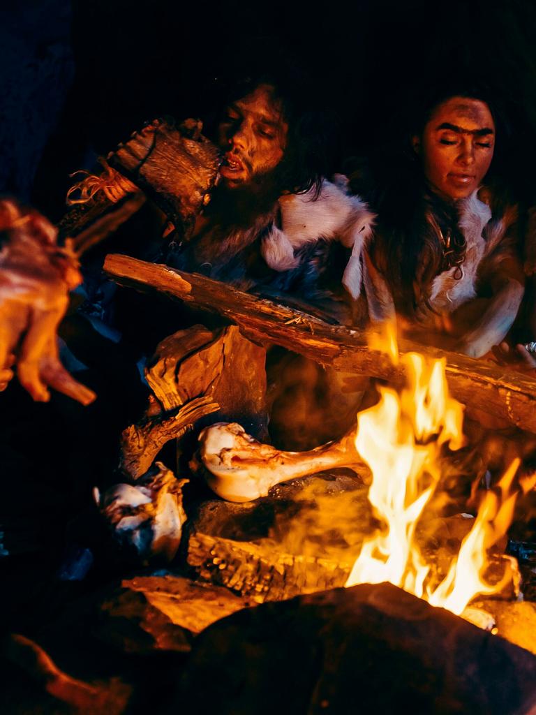 Neandertaler braten über einem offenen Feuer Fleisch in einer Höhle.