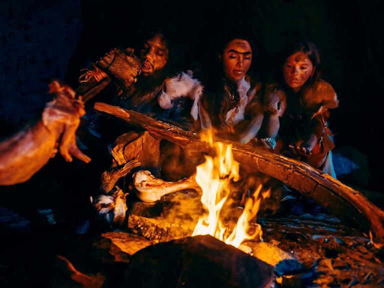 Neandertaler braten über einem offenen Feuer Fleisch in einer Höhle.