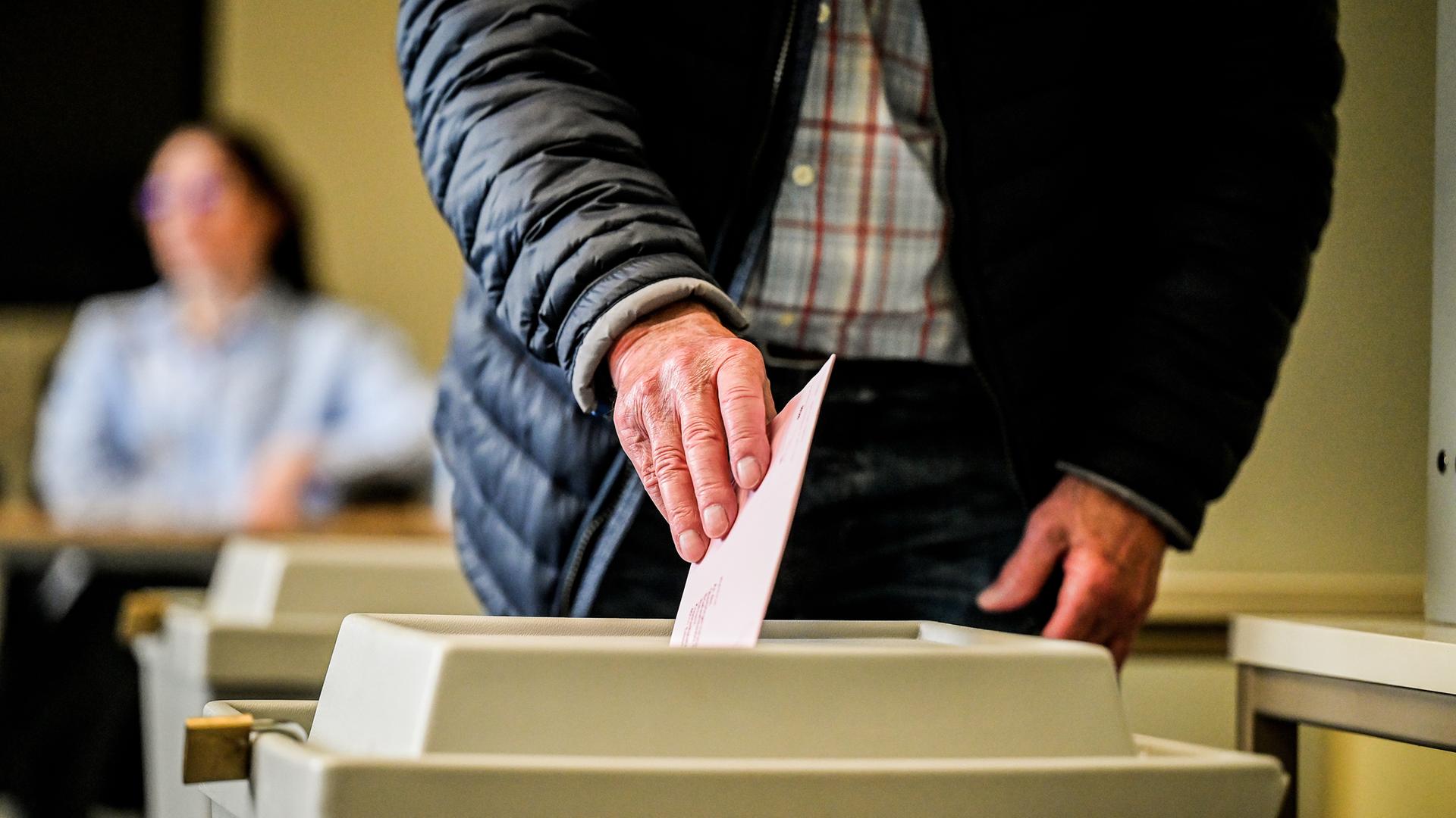 Eine sichtbar alte Hand wirft einen Wahlzettel in die Urne.