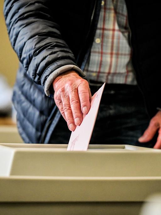 Eine sichtbar alte Hand wirft einen Wahlzettel in die Urne.