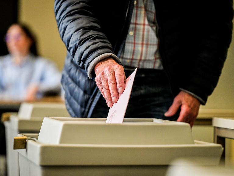 Eine sichtbar alte Hand wirft einen Wahlzettel in die Urne.