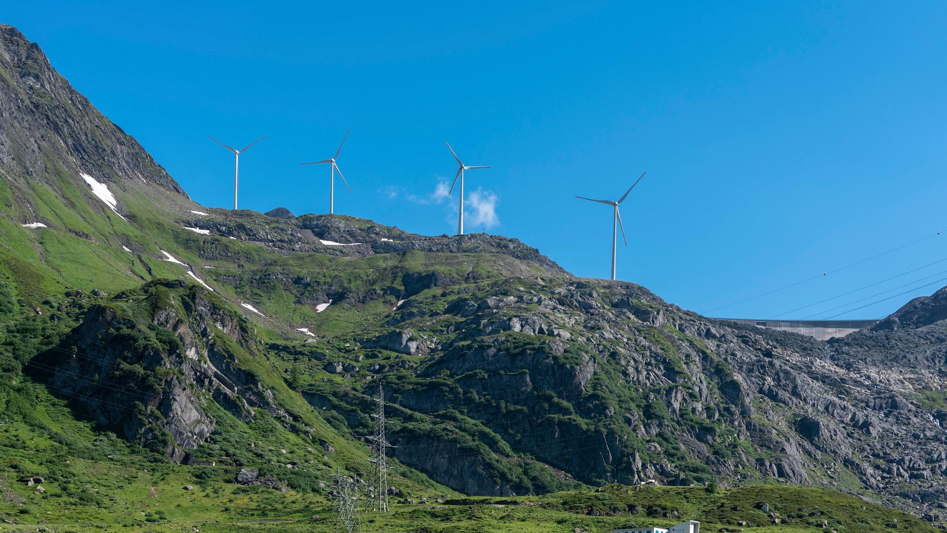 Vier Windräder stehen auf einem felsigen Berg vor blauem Himmel. Vier Windräder stehen auf einem felsigen Berg vor blauem Himmel.