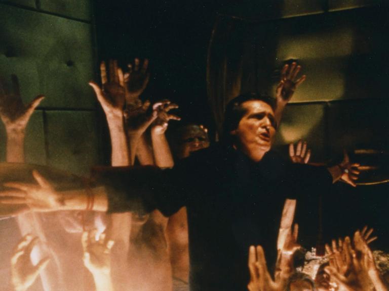 Szene aus dem Film "Der Exorzist III": Hände griefen nah einem cMann am Kreuz