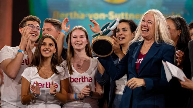 Mehrere Schülerinnen, Schüler und Lehrkräfte von der Gesamt-Schule in Mörfelden-Walldorf stehen nebeneinander und lachen. Die Schulleiterin (r.) hält den Deutschen Schulpreis in den Händen.
