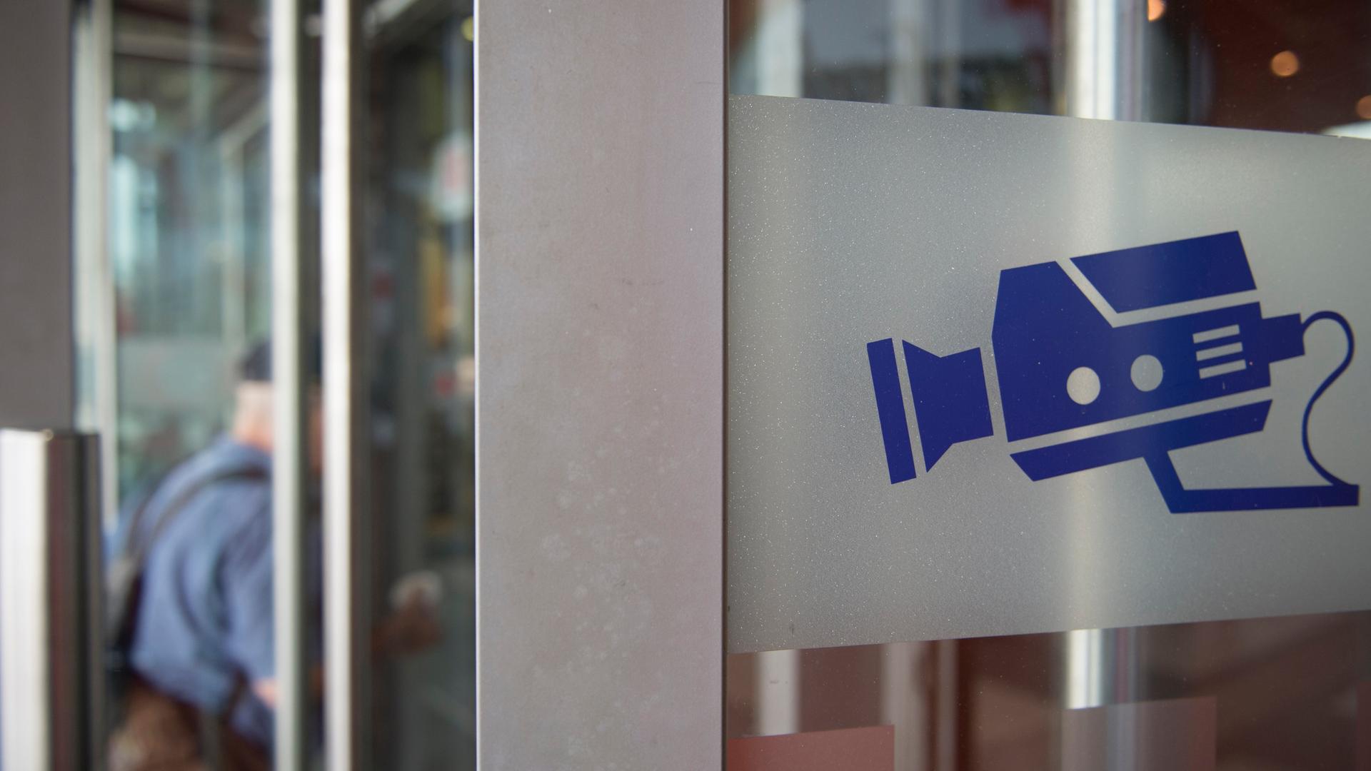 Auf einem Hinweisschild ist eine Kamera abgebildet, aufgenommen an einer Eingangstür am Bahnhof Auf einem Hinweisschild ist eine Kamera abgebildet, aufgenommen an einer Eingangstür am Bahnhof