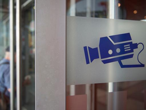 Auf einem Hinweisschild ist eine Kamera abgebildet, aufgenommen an einer Eingangstür am Bahnhof