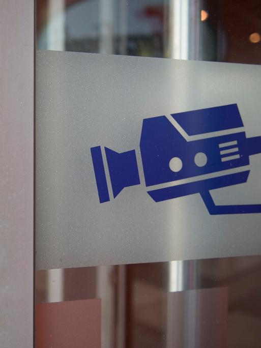 Auf einem Hinweisschild ist eine Kamera abgebildet, aufgenommen an einer Eingangstür am Bahnhof