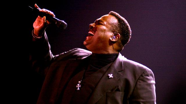 Luther Vandross trägt ein schwarzes Rollkragenshirt und einen dunklen Anzug und singt 2002 auf der Bühne der Sheffield Arena aus voller Brust in ein Mikrofon