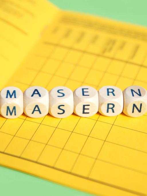 Symbolbild: Scrabblewürfel zeigen das Wort "Masern". Sie liegen auf einem gelben Impfpass aus Deutschland. 