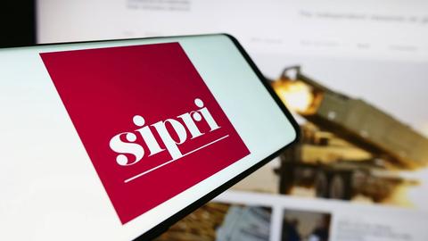 Mobiltelefon mit dem Logo des Stockholm International Peace Research Institute SIPRI vor einer Website. 