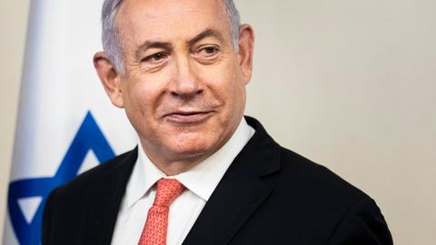 Der israelische Ministerpräsident Benjamin Netanjahu blickt nach rechts aus dem Bild, im Hintergrund ist eine israelische Flagge.