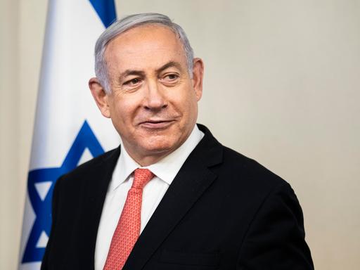 Der israelische Ministerpräsident Benjamin Netanjahu blickt nach rechts aus dem Bild, im Hintergrund ist eine israelische Flagge.