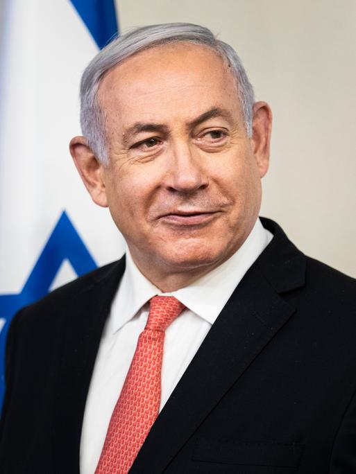 Der israelische Ministerpräsident Benjamin Netanjahu blickt nach rechts aus dem Bild, im Hintergrund ist eine israelische Flagge.