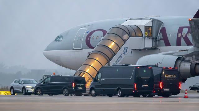 Auf dem Foto sieht man den vorderen Teil eines Flugzeugs Daran ist eine Treppe angelehnt. Über die Treppe gehen Menschen in das Flugzeug. Vor dem Flugzeug parken mehrere große, schwarze Autos.