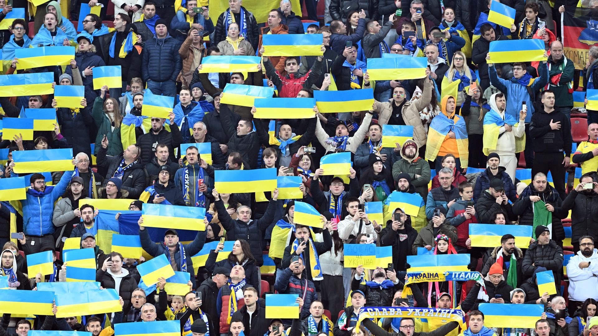 Ukraine Fans halten beim Fußballspiel zwischen der Ukraine und Italien ukrainische Flaggen in die Luft. 