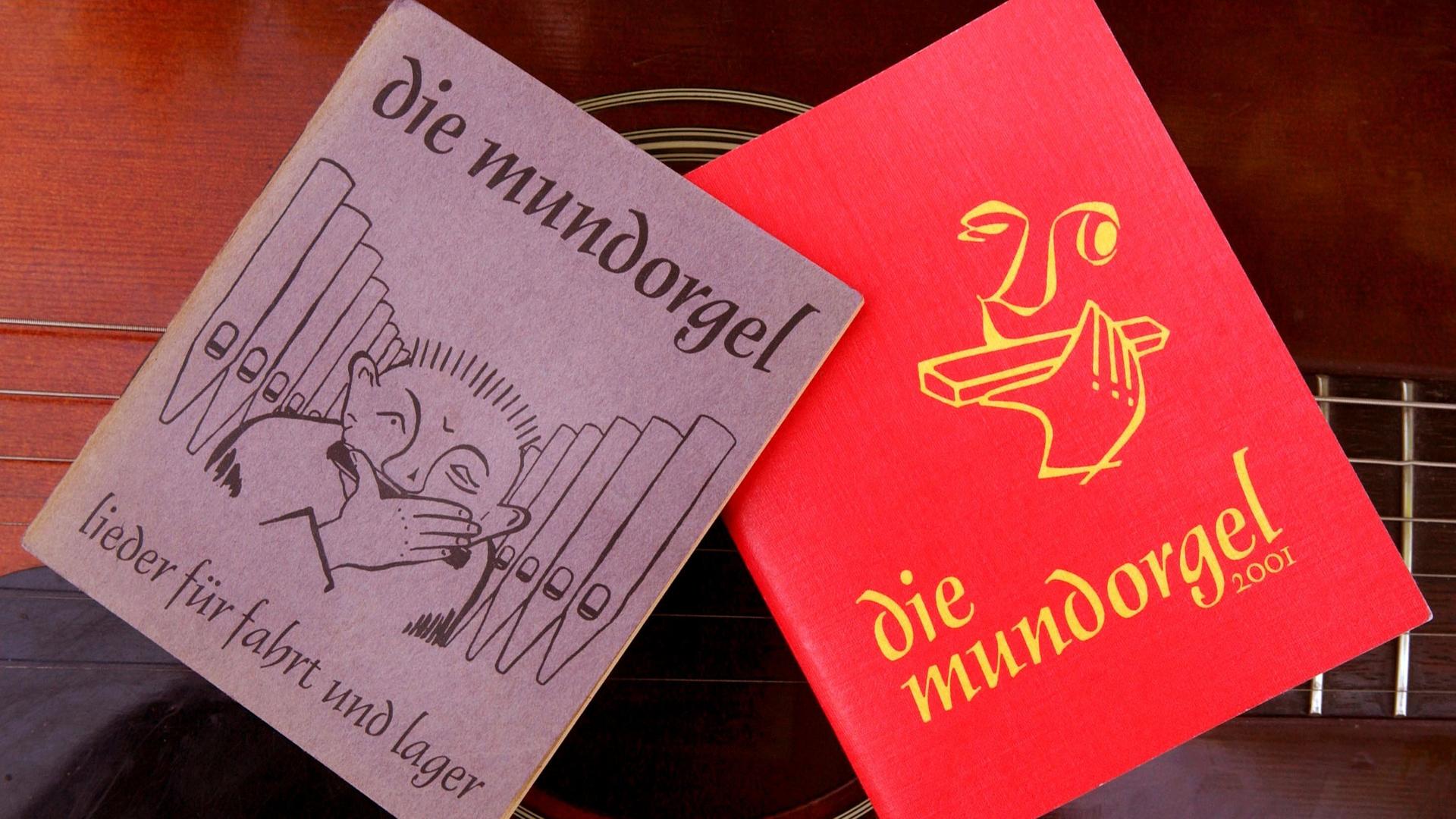 Eine moderne Ausgabe von 2001 und eine der ersten Ausgaben der "Mundorgel" aus den 1950er Jahren liegen auf einer Gitarre. Das "Liederbuch für Fahrt und Lager" gibt es seit 70 Jahren.