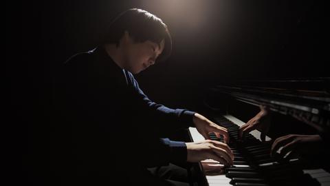 Ein junger japanischer Pianist sitzt an einem Flügel. Er spielt und blickt versonnen auf die Tasten.