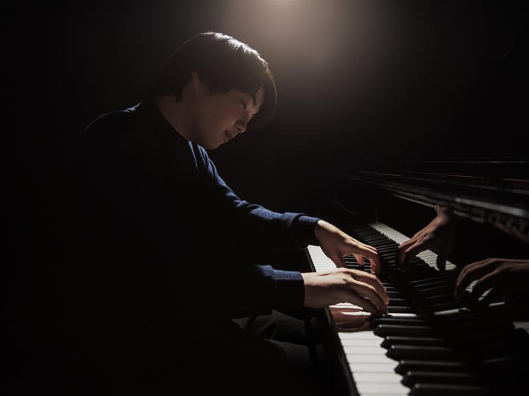 Ein junger japanischer Pianist sitzt an einem Flügel. Er spielt und blickt versonnen auf die Tasten.