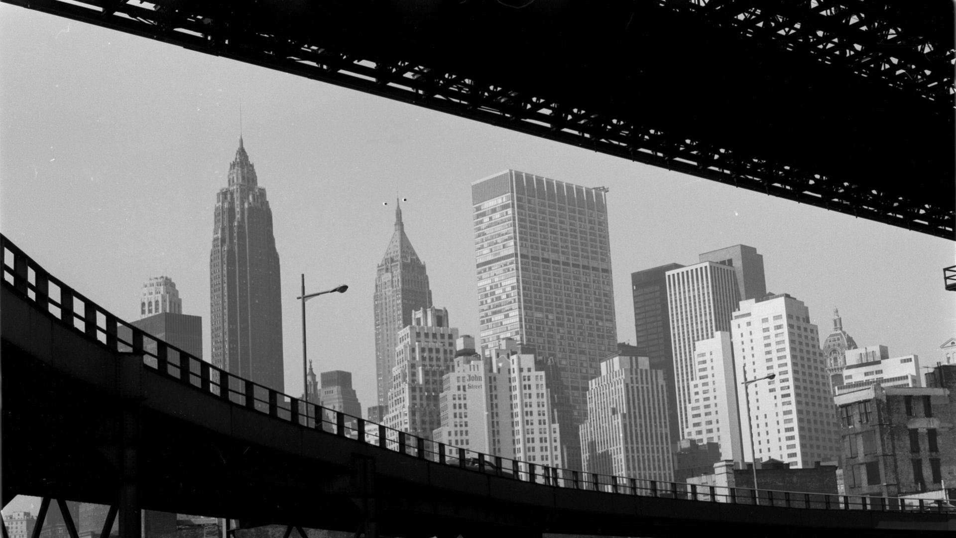 Ein schwarz weiß Foto von New York, in den USA, um 1959. Der Blick geht durch zwei Brücken auf Hochkratzer.