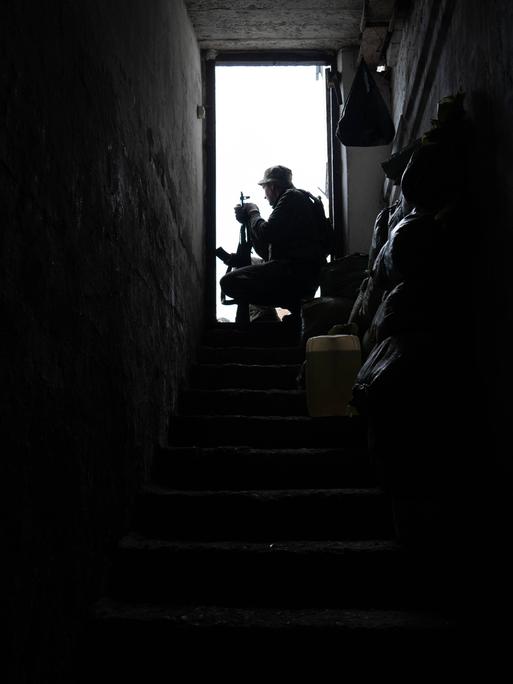 Ein ukrainischer Soldat sitzt an einer geöffneten Tür am Ende einer langen Treppe, der Raum ist dunkel, die Szene ist von einem Stützpunkt nahe Soledar, in der Donezk Region, 25. April 2023