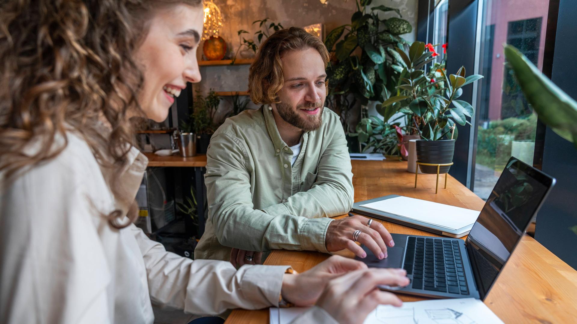 Eine Frau und ein Mann arbeiten in einem Café zusammen am Laptop. 