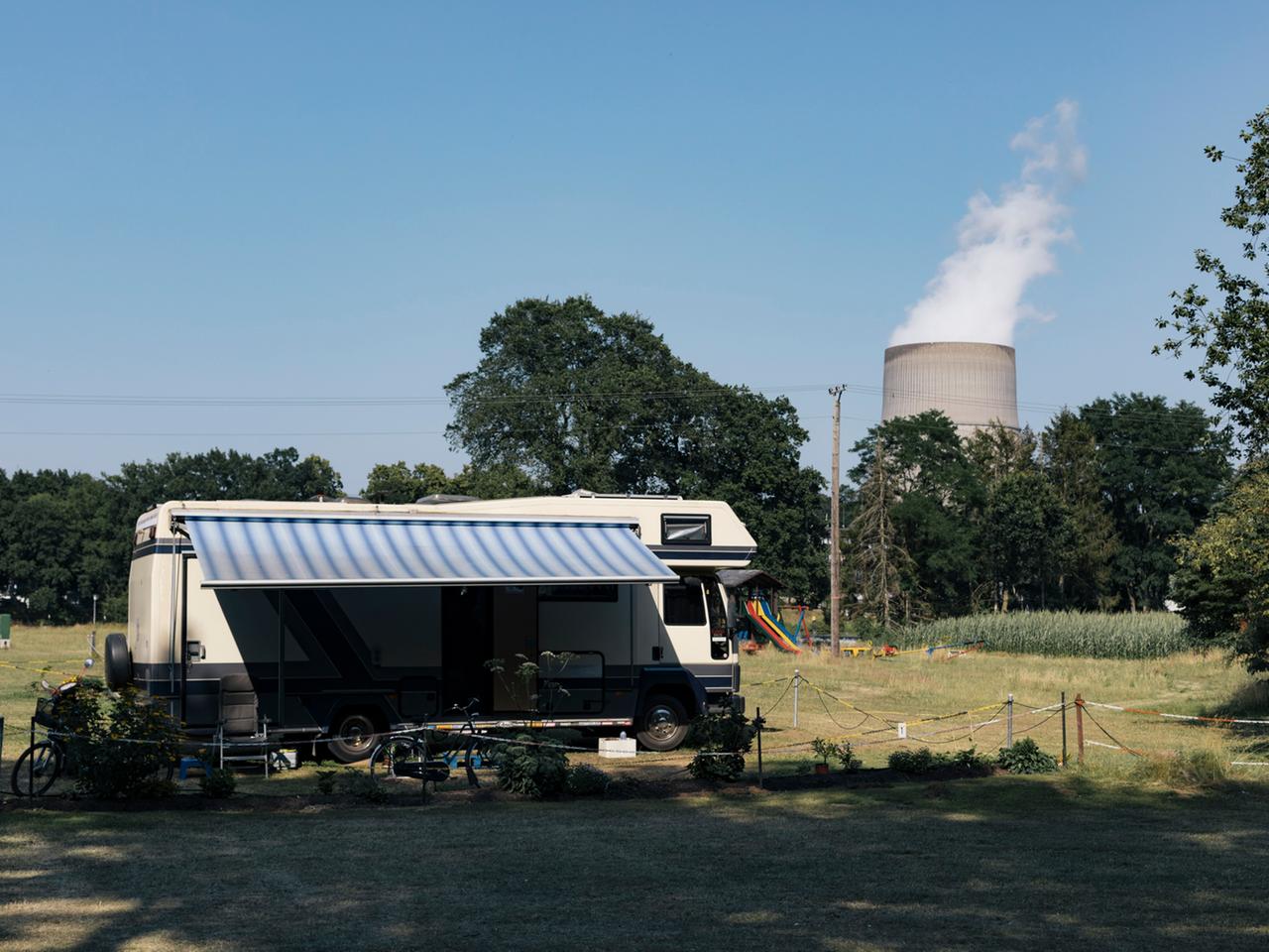 Sommer. Ein Camper steht auf einer Wiese, im Hintergrund ist der Kühlturm des Atomkraftwerks in Lingen (Ems) zu sehen.