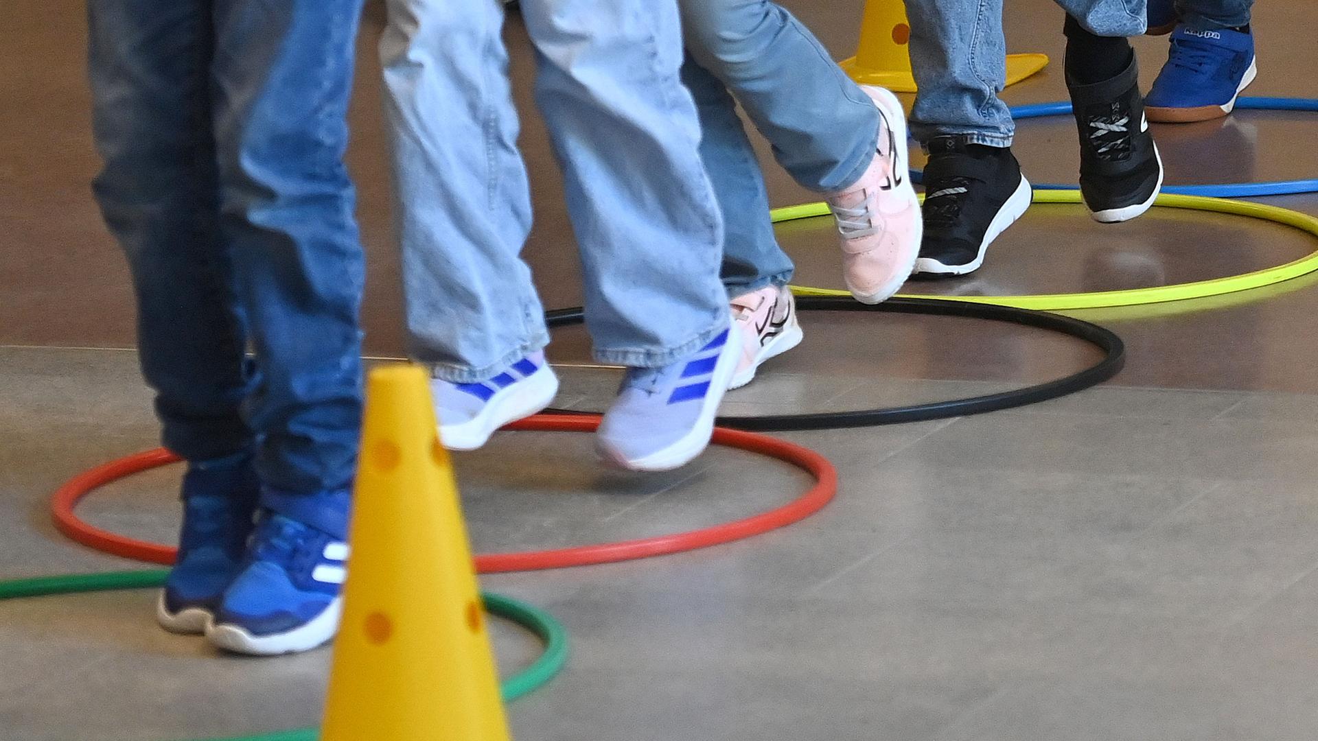 Mehrere Kinderbeine in Turnschuhen während des Sportunterrichts. Sie hüpfen über Reifen, die auf dem Boden liegen. Mehrere Kinderbeine in Turnschuhen während des Sportunterrichts. Sie hüpfen über Reifen, die auf dem Boden liegen.