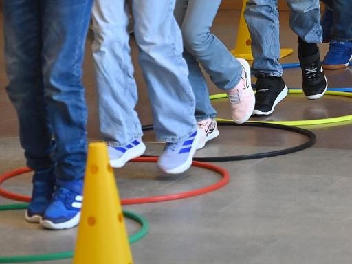 Mehrere Kinderbeine in Turnschuhen während des Sportunterrichts. Sie hüpfen über Reifen, die auf dem Boden liegen. Mehrere Kinderbeine in Turnschuhen während des Sportunterrichts. Sie hüpfen über Reifen, die auf dem Boden liegen.